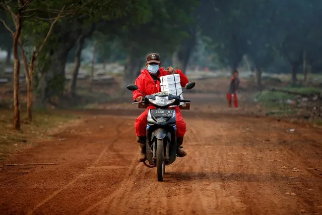 A worker wearing a protective suit rides a motorbike carrying boxes of meals near the Muslim burial area provided by the government for victims of the coronavirus at Pondok Ranggon cemetery complex in Jakarta, Indonesia, August 5, 2020. (Photo by Willy Kurniawan/Reuters)