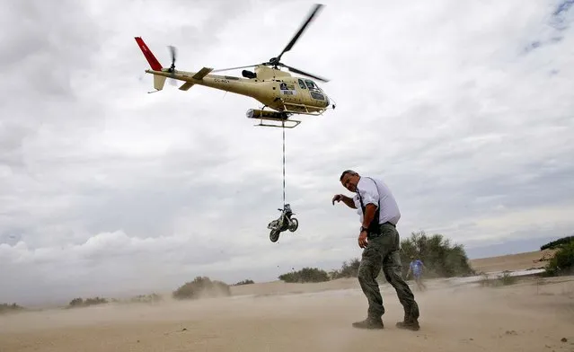 Dakar Rally Director Etienne Lavigne covers as sand is kicked up by a helicopter lifting the motorcycle of Herve Thierry of France after it fell in a river during the 11th stage of the 2013 Dakar Rally, January 16, 2013. (Photo by Bertrand Metayer/ Le Parisien)