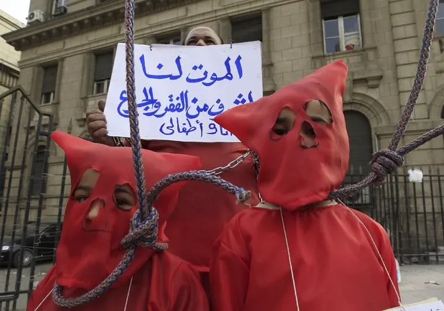 A man holds a sign behind his children portraying an execution with hoods over their heads and nooses around their necks, during an anti-government protest in Cairo February 22, 2013. President Mohamed Mursi on Thursday called parliamentary elections that will begin on April 27 and finish in late June, a four-stage vote that the Islamist leader hopes will conclude Egypt's turbulent transition to democracy. The sign reads, “Death is more honorable than poverty and hunger for me and my children”. (Photo by Mohamed Abd El Ghany/Reuters)