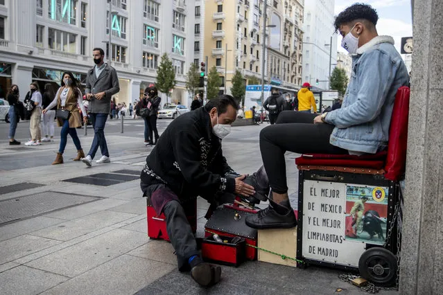 A shoe shiner wearing a face mask to prevent the spread of coronavirus cleans a shoes of a customer at Gran Via avenue in downtown Madrid, Spain, Saturday, September 26, 2020. Spain's health minister has reiterated his plea for Madrid's regional authorities to apply more stringent restrictions on mobility in Europe's worst coronavirus hotspot. (Photo by Manu Fernandez/AP Photo)