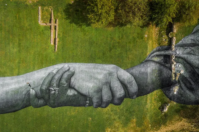 An aerial picture taken with a drone shows French artist Saype posing by his giant biodegradable land art painting of interlocked hand, as part of “Beyond Walls”, his project creating a spray-painted “human chain” across the world to encourage humanity and equality, by the ancient Palatine Gate in Turin, Italy, September 29, 2020. (Photo by Valentin Flauraud for Saype/Handout via Reutsr)