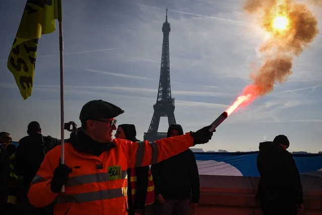 A members of the SUD labour union holds a flare during a demonstration on the Parvis du Trocadero, across the Seine river from the Eiffel Tower, during a cross-sector labour union protest against France's controversial pension reform bill, in Paris, on February 9, 2023. The planned reforms include hiking the retirement age from 62 to 64 and increasing the number of years people must make contributions for a full pension. (Photo by Alain Jocard/AFP Photo)