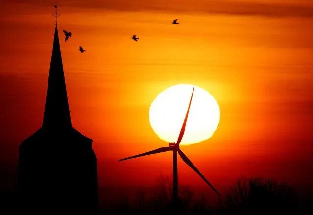 A power-generating windmill turbine and the church of the village are pictured during sunrise at a wind park in Rieux-en-Cambresis, France on December 18, 2022. (Photo by Pascal Rossignol/Reuters)