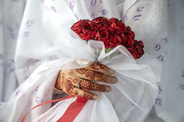 An Afghan bride holds a bouquet of roses at a mass wedding ceremony, during the International Women's Day in Kabul, Afghanistan, Wednesday, March 8, 2023. (Photo by Ebrahim Noroozi/AP Photo)
