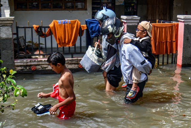 A resident carries a child during flooding in Bojongasih Village, Dayeuhkolot, Bandung Regency, West Java on October 24, 2025. Heavy rains that hit Bandung from Thursday, October 23, from afternoon to evening, left hundreds of homes and roads in Bandung Regency submerged in floodwaters up to 40 centimeters deep. (Photo by Dimas Rachmatsyah/ZUMA Press Wire/Rex Features/Shutterstock)