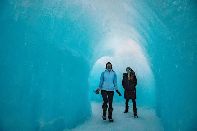 People walk through an ice tunnel as they explore the ice walls, tunnels and lights at Ice Castles in North Woodstock, New Hampshire, on January 14, 2021. Hundreds of people attended the sold out opening night that was delayed by two weeks due to warm weather and rain. (Photo by Joseph Prezioso/AFP Photo)