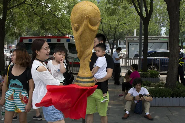 Huang Xin seated bottom right waits near the replica trophy he made from human hair in the likeness of the FIFA World Cup to coincide with the 2018 soccer World Cup held in Russia on the streets of Beijing, China, Monday, June 18, 2018. According to the artist Huang Xin, 2.18 kg. (4.8 lb.) of human hair from as many as 56 ethnicities in China collected over the past four years were used in the creation of the trophy. (Photo by Ng Han Guan/AP Photo)