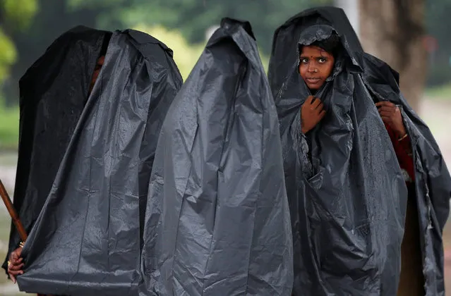 Women cover themselves with plastic sheets as it rains in New Delhi, India, July 26, 2018. (Photo by Adnan Abidi/Reuters)