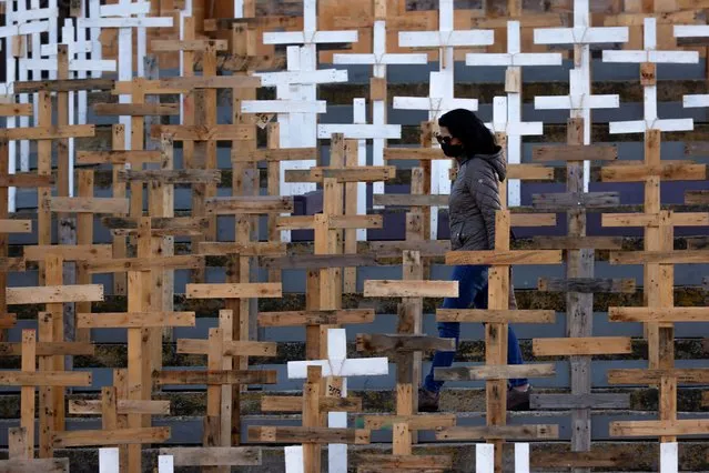 A woman wearing a mask walks among hundreds of crosses set up in front of the Parish Church of Our Lady of Loreto to commemorate Holy Week and as a memorial to the victims of the coronavirus disease (COVID-19) pandemic, in the village of Ghajnsielem on the island of Gozo, Malta on March 27, 2021. (Photo by Darrin Zammit Lupi/Reuters)
