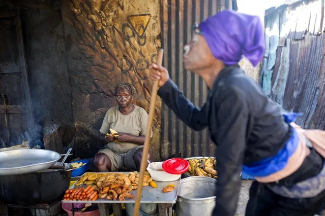 In this October 27, 2018 photo, Atesi Auguste, a voodoo priestess, sits as she sells fried meat and bananas and she watches Mimose Bernard who issupposed to be possessed the Gede spirit, during Haiti's annual Voodoo festival Fete Gede, in Cite Soleil slum, in Port-au-Prince, Haiti. “I have thirty years in having Gede spirit manifested in my head”, said Auguste. (Photo by Dieu Nalio Chery/AP Photo)