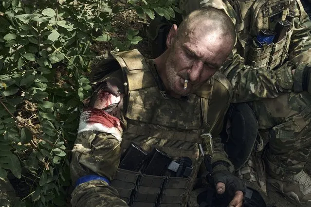 A wounded soldier of Ukraine's 3rd Separate Assault Brigade smokes as he waits for evacuation near Bakhmut, the site of fierce battles with the Russian forces in the Donetsk region, Ukraine, Monday,  September 4, 2023. (Photo by Libkos/AP Photo)