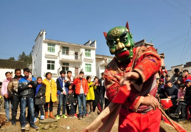 People watch a man wearing a mask perform a ritual dance named “Nuo” at the beginning of the Chinese Lunar New Year, in Wuyuan, Jiangxi province, February 9, 2016. (Photo by Reuters/Stringer)