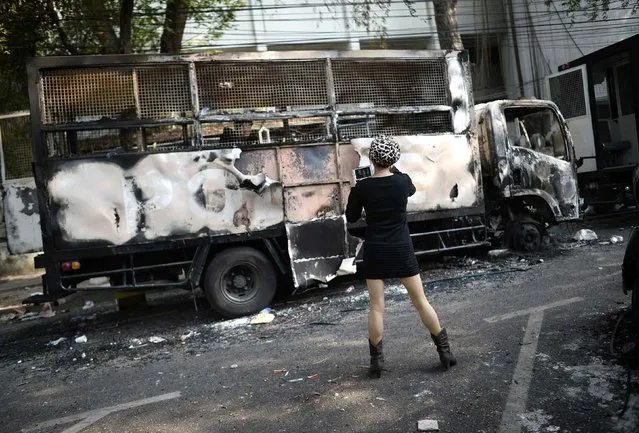 A woman takes pictures of a burnt out police truck after anti-government protesters called off demonstrations outside Government House in Bangkok December 3, 2013. Thailand's government ordered police to stand down and allow protesters into state buildings on Tuesday, removing a flashpoint for clashes and effectively bringing an end to days of violence in Bangkok in which five people have died. (Photo by Dylan Martinez/Reuters)