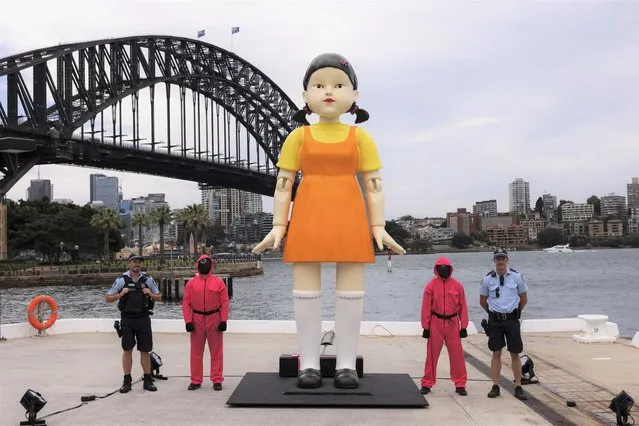 Police pose next to a replica animated doll from the series the Squid Games on October 29, 2021 in Sydney, Australia. The replica animated doll from the Netflix series Squid Game has been installed at Sydney Harbour for Halloween. The doll, which is 4.5 metres tall and weighs three tonnes, can turn its head and chants “red light, green light”. Sydneysiders are invited to play the popular Korean children's game made popular by the television show. (Photo by Brook Mitchell/Getty Images)