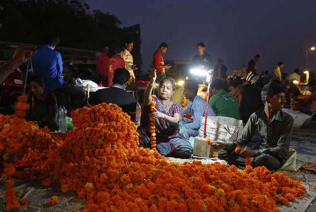 A vendor (C) makes a garland with marigold flowers as she waits for customers during early morning at a wholesale flower market in Ahmedabad, November 25, 2014. (Photo by Amit Dave/Reuters)
