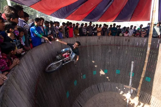Daring motorists entertain spectators by dangerously driving motorcycles on a vertical “wall of death” in Khulna, Bangladesh on January 30, 2024. Performers travel without protective gears at speeds of up to 80 km/h so that their vehicles can balance on the 25-foot-high wooden plank. Riders pull off death-defying stunts to wow bystanders in an attempt to make extra money as they ride vertically up the side of a wall. They perform to entertain those who have paid an entry fee of 20 pence for the entertainment. Up to 100 spectators can watch at a time offering up money to the riders so they can earn extra money from these tips. (Photo by Joy Saha/ZUMA Press Wire/Rex Features/Shutterstock)