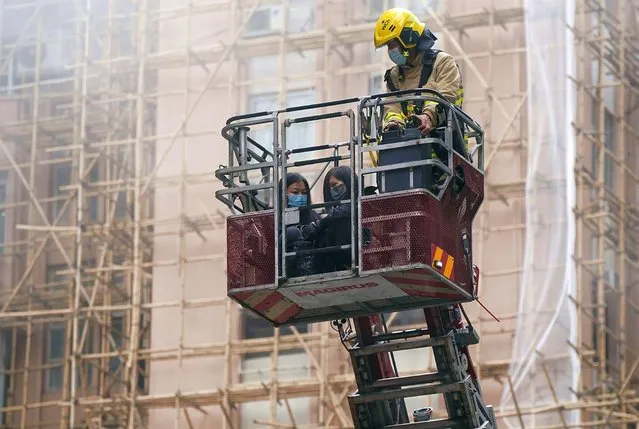 Two women are rescued by a firefighter in a bucket crane outside the World Trade Centre located in the city's popular Causeway Bay shopping district of Hong Kong, Wednesday, December 15, 2021. (Photo by AP Photo/Stringer)
