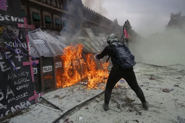 A demonstrator throws burning gasoline at a police shield wall that is closing a breach on a barricade protecting the National Palace during a march to commemorate International Women's Day and protest against gender violence, in Mexico City, Monday, March 8, 2021. (Photo by Ginnette Riquelme/AP Photo)