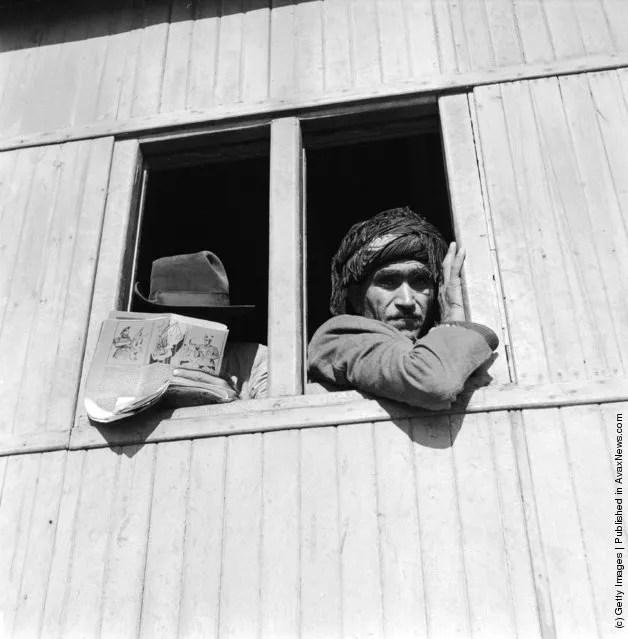 1952:  Third class rail travellers on the train through the Luristan region, Iran. A man on the left is reading a magazine with an anti-Soviet cartoon depicting red Russia about to sever China's head with its symbolic sickle as the world protests in vain