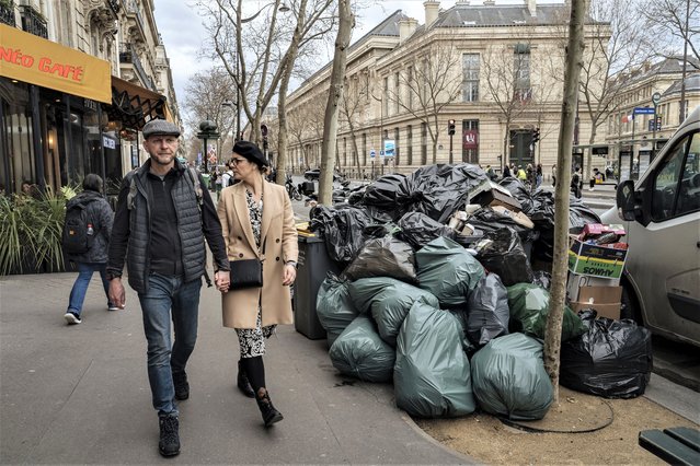 People walk past uncollected garbage in Paris, Monday, March 13, 2023. A contentious bill that would raise the retirement age in France from 62 to 64 got a push forward with the Senate's adoption of the measure amid strikes, protests and uncollected garbage piling higher by the day. (Photo by Lewis Joly/AP Photo)
