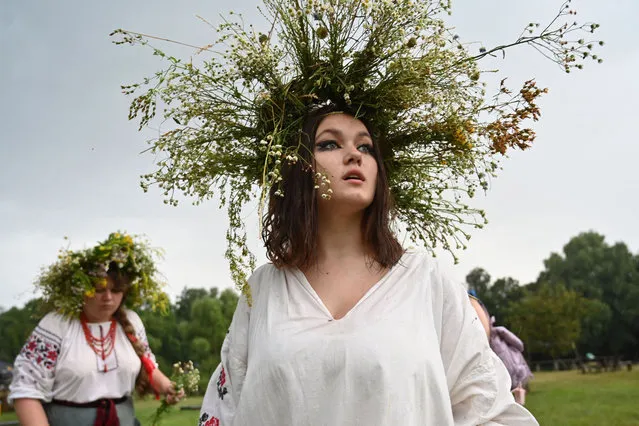 A woman reacts after she mades a wreath of flowers during the celebrations of the Kupala night in Pyrohiv, near Kiev, on July 6, 2021. During the celebration, an ancient slavic ritual related to the summer solstice, people wear wreaths, jump over fires and bathe naked in rivers and lakes. (Photo by Sergei Supinsky/AFP Photo)