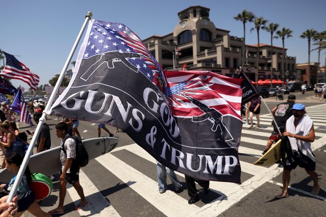 A pro-Trump supporter waves a flag reading ”God Guns and Trump” during a demonstration in support of former President Donald Trump who was shot the previous day in an assassination attempt during a rally in Pennsylvania, in Huntington Beach, California on July 14, 2024. (Photo by Etienne Laurent/Reuters)