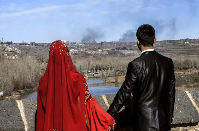 A couple hold hands for a wedding photo as they look at smokes rising over the district of Sur in Diyarbakir on February 3, 2016 after clashes between Kurdish rebels and Turkish forces. (Photo by Ilyas Akengin/AFP Photo)