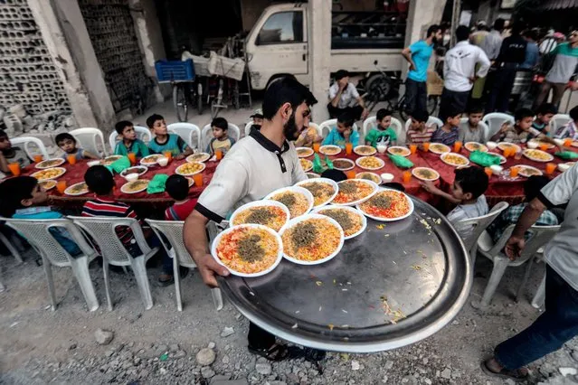A man carries plates with food in preparation for Iftar, evening meal at the end of daily Ramadan fast at sunset, next to rubble and destroyed houses, which were damaged after air strikes, in Douma, Syria, 17 June 2017. Muslims around the world celebrate the holy month of Ramadan by praying during the night time and abstaining from eating, drinking, and sexual acts daily between sunrise and sunset. Ramadan is the ninth month in the Islamic calendar and it is believed that the Koran's first verse was revealed during its last 10 nights. (Photo by Mohammed Badra/EPA)