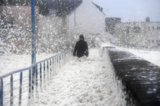 A person walks as sea foam washes up on the the frontwalk in Saint-Guenole, western France, as storm Dennis sweeps accross Brittany, on February 16, 2020. (Photo by Fred Tanneau/AFP Photo)