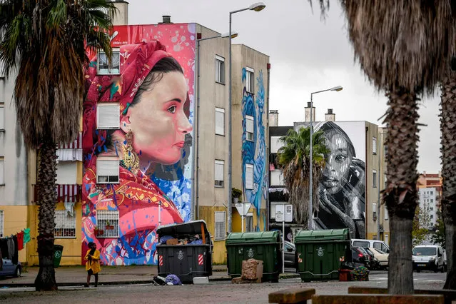 A resident of Quinta do Mocho neighbourhood walks past murals by Liberian artist Arcy (L) and Portuguese artist Huariu, in Sacavem, outskirts of Lisbon, on November 11, 2019. (Photo by Patricia De Melo Moreira/AFP Photo)