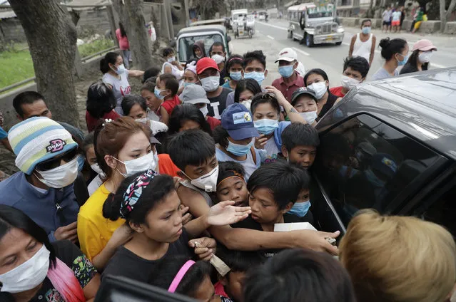 Residents scramble to grab relief goods given by a citizen at a town near Taal volcano, Tagaytay, Cavite province, southern Philippines on Sunday January 19, 2020. Many poor families living near Taal volcano have been affected due to loss of income after business closures in the area. (Photo by Aaron Favila/AP Photo)