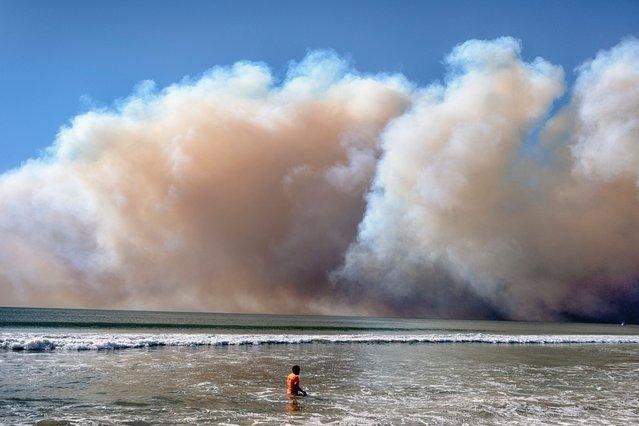 A swimmer watches as a large dark plume of smoke passes over the beach from a wildfire from Pacific Palisades, in Santa Monica, Calif., Tuesday, January 7, 2025. (Photo by Richard Vogel/AP Photo)