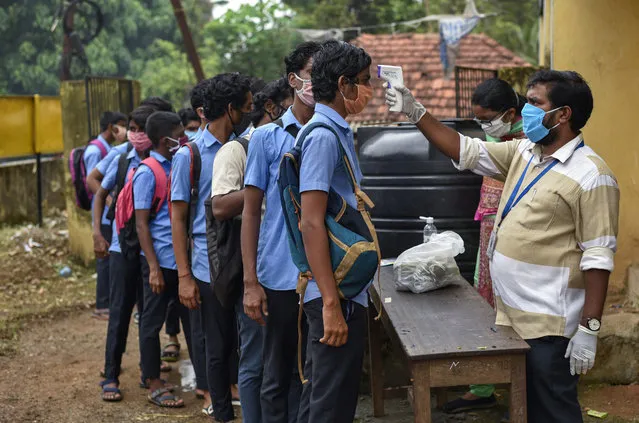 School children wearing masks line up to get their hands sanitized and temperatures checked as they arrive to appear for state board examination during the coronavirus pandemic in Kochi, Kerala state, India, Tuesday, May 26, 2020. (Photo by R.S. Iyer/AP Photo)