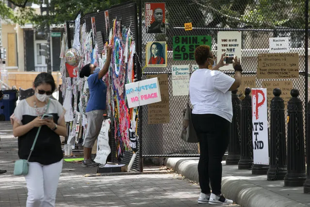 People look at protest posters that adorn the last remaining anti-scaling fencing surrounding a small building in Lafayette Park, Tuesday, June 16, 2020, near the White House in Washington, where protests have occurred over the death of George Floyd, a black man who was in police custody in Minneapolis. The rest of the park is open. (Photo by Jacquelyn Martin/AP Photo)