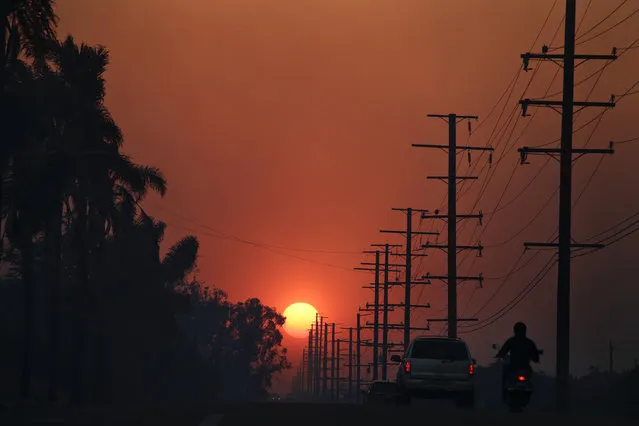 The sun is seen through thick smoke generated by a wildfire Tuesday, Dec. 5, 2017, in Santa Paula, Calif. Raked by ferocious Santa Ana winds, explosive wildfires northwest of Los Angeles and in the city's foothills burned a psychiatric hospital and scores of homes and other structures Tuesday and forced the evacuation of tens of thousands of people. (Photo by Jae C. Hong/AP Photo)