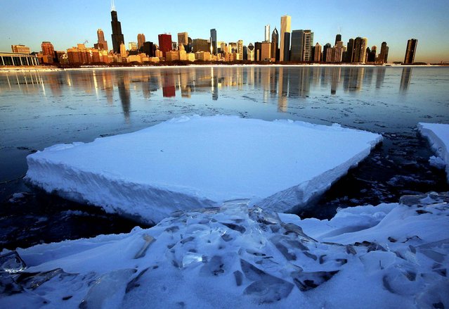 The Chicago skyline is reflected on a thin layer of ice as a chunk of snow-covered ice floats in Monroe Harbor one day after a blizzard dumped the third largest snowfall in Chicago's history. (Photo by Charles Rex Arbogast/Associated Press)