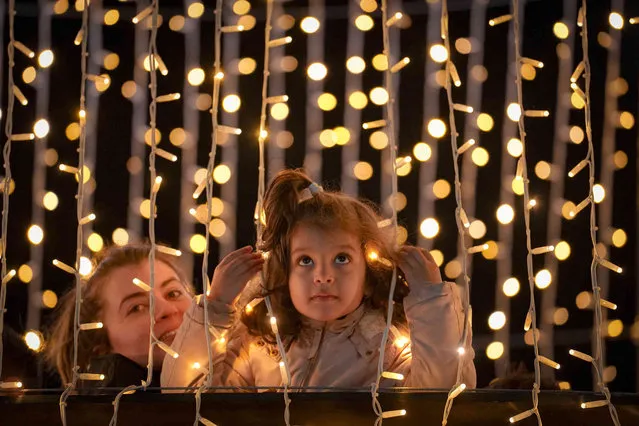 A girl peers from between light decorations at a Christmas fair which opened ahead of the holiday season in Bucharest, Romania, Friday, November 25, 2022. Municipal authorities in the Romanian capital, quoted by local media, stated that holiday season city light decoration levels will remain at last year's level and use energy saving solutions. (Photo by Vadim Ghirda/AP Photo)
