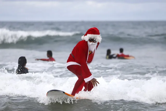 A Balinese man dressed as Santa Claus teaches orphan children how to surf at a beach in Kuta, Bali, Indonesia December 7, 2014. Every year in December a surf school in Bali held a free surf lesson to orphans as a part of Christmas celebration. (Photo by Made Nagi/EPA)