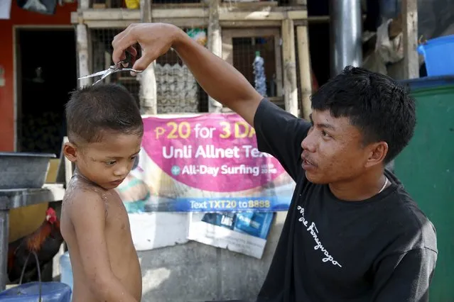 A father cuts his son's hair outside their bunkhouse at a transitional shelter for Typhoon Haiyan survivors in Tacloban city November 1, 2015,  ahead of the second anniversary of the devastating typhoon that killed more than 6000 people in central Philippines. (Photo by Erik De Castro/Reuters)