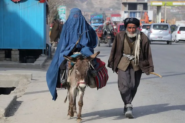 A man walks beside a burqa-clad woman riding a donkey along a street in Fayzabad on March 8, 2023. (Photo by Omer Abrar/AFP Photo)