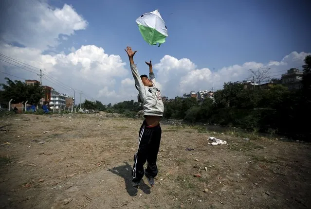 A boy helps his friend (unseen) to fly a kite during Dashain, the biggest religious festival for Hindus in Nepal, in Kathmandu, October 15, 2015. Hindus in Nepal celebrate victory over evil during the festival by flying kites, feasting, playing on swings, sacrificing animals and worshipping the Goddess Durga as well as other gods and goddesses as part of celebrations held throughout the country. (Photo by Navesh Chitrakar/Reuters)