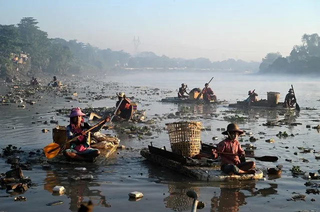 This photo taken on January 14, 2023 shows waste collectors paddling polystyrene boats as they look for plastic and glass to recycle in Pazundaung Creek in Yangon. Dozens of Myanmar waste collectors are taking to the murky waters of a Yangon creek after being driven to find work by a post-coup economic crisis. (Photo by Sai Aung Main/AFP Photo)