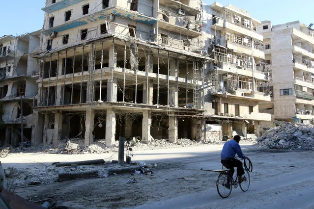 A man rides a bicycle near damaged buildings in the rebel held besieged al-Sukkari neighbourhood of Aleppo, Syria October 19, 2016. (Photo by Abdalrhman Ismail/Reuters)