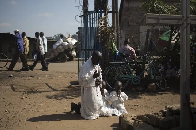 A member of the Legio Maria and his children pray by a cross near the gate of their church during Sunday mass in Korogocho, Nairobi, Kenya, July 5, 2015. Legio Maria was founded in Kenya in the 1960s. Followers worship a black messiah, the church's founder, who they believe is a reincarnation of Jesus Christ. (Photo by Siegfried Modola/Reuters)