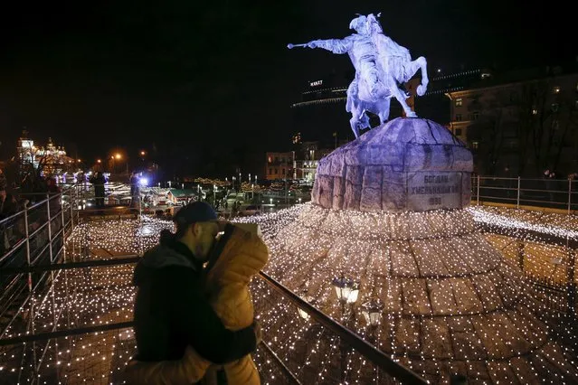 A couple kisses in front of the monument “Bogdan Khmelnitsky”, a 17th century Cossack leader, decorated with festive illumination lights for the New Year and Christmas holidays celebrations, in central Kiev, Ukraine, December 22, 2015. (Photo by Valentyn Ogirenko/Reuters)