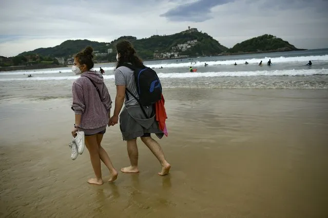 A couple walk along La Concha beach, after lockdown restrictions were lifted, in San Sebastian, northern Spain, Sunday, May 9, 2021. Impromptu street celebrations erupted across Spain as the clock struck midnight on Saturday, when a six-month-long national state of emergency to contain the spread of coronavirus ended and many nighttime curfews were lifted. (Photo by Alvaro Barrientos/AP Photo)