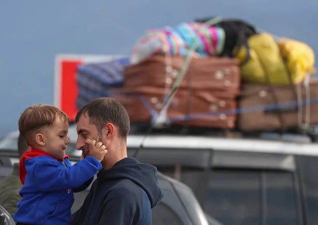 A refugee from Nagorno-Karabakh region holds a child while standing next to a car upon their arrival in the border village of Kornidzor, Armenia on September 26, 2023. (Photo by Irakli Gedenidze/Reuters)