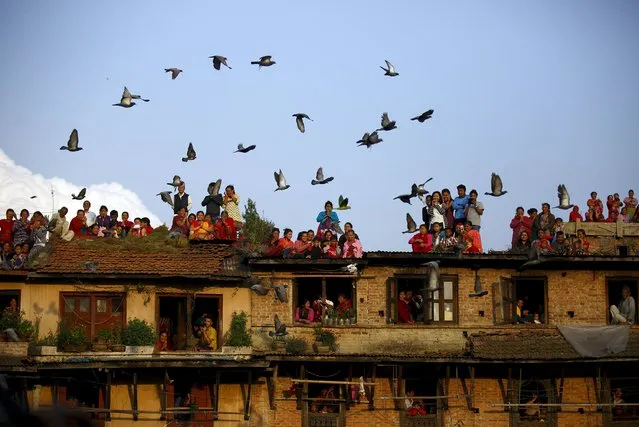 Pigeons fly past devotees gathering on the roof of the houses to observe religious rituals of Rato Machhindranath at Bungamati in Lalitpur April 5, 2015. Rato Machhindranath is known as the god of rain and both Hindus and Buddhists worship Machhindranath for good rain to prevent drought during the rice harvest season. (Photo by Navesh Chitrakar/Reuters)