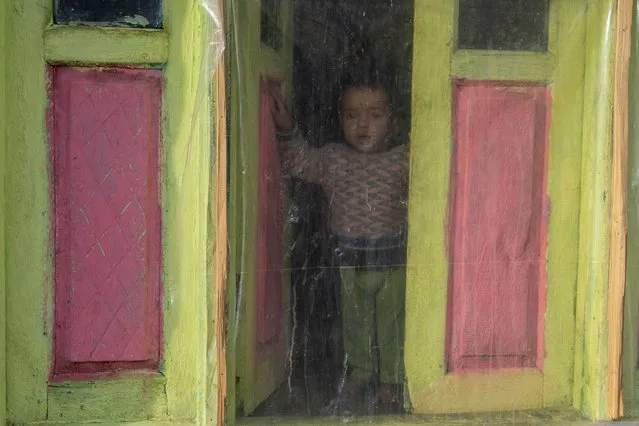 A Kashmiri villager boy looks out of a window covered with a plastic sheet, used as a shield against the cold, in Drang village northwest of Srinagar, Indian controlled Kashmir Friday, December 22, 2023. (Photo by Dar Yasin/AP Photo)