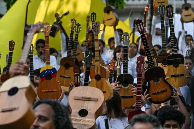 Students lift their cuatro during the national day of the musical instrument at Bolivr Square in Caracas on April 4, 2024. The cuatro is a four-stringed instrument of colonial origin in the guitar family that is used in all folkloric rhythms of Venezuela and Colombia. (Photo by Juan Barreto/AFP Photo)